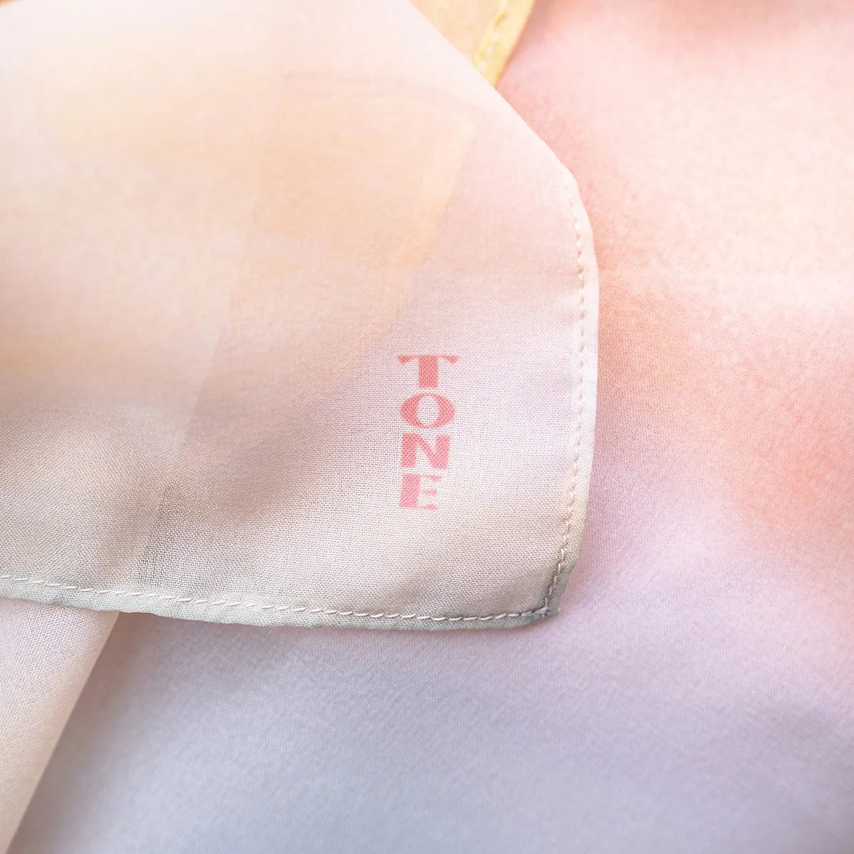 淡い暖色グラデーションのTONEオリジナルスカーフのロゴアップ写真